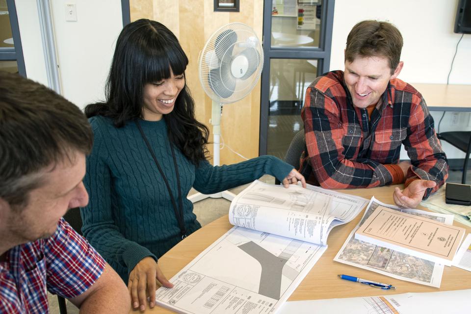 Hands reviewing engineering plans spread across a table
