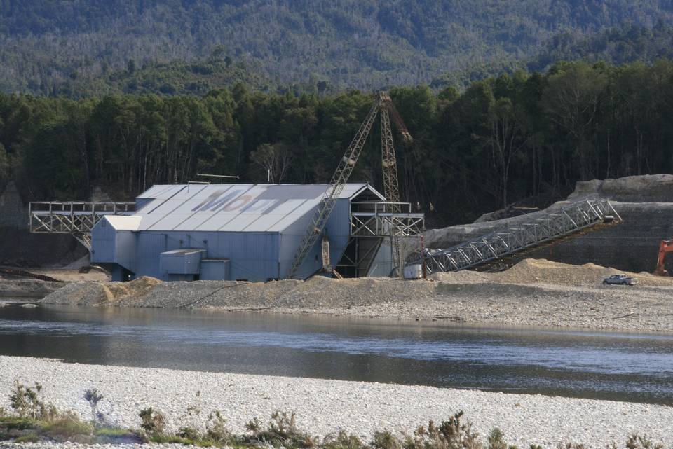 A floating gold dredge working a river between forested banks